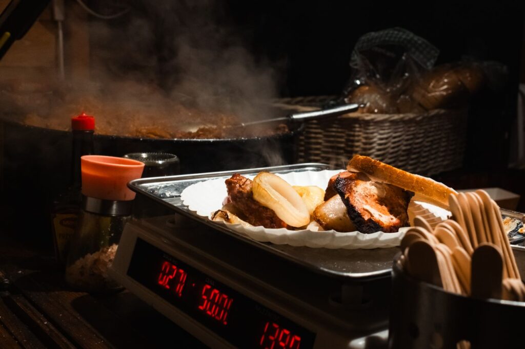 Close-up of a steaming grilled meat platter with bread and potatoes at a German market stall.