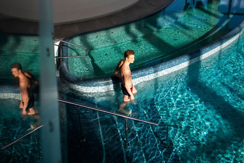 A man wades in a sunlit swimming pool, enjoying a relaxing moment with light reflections.
